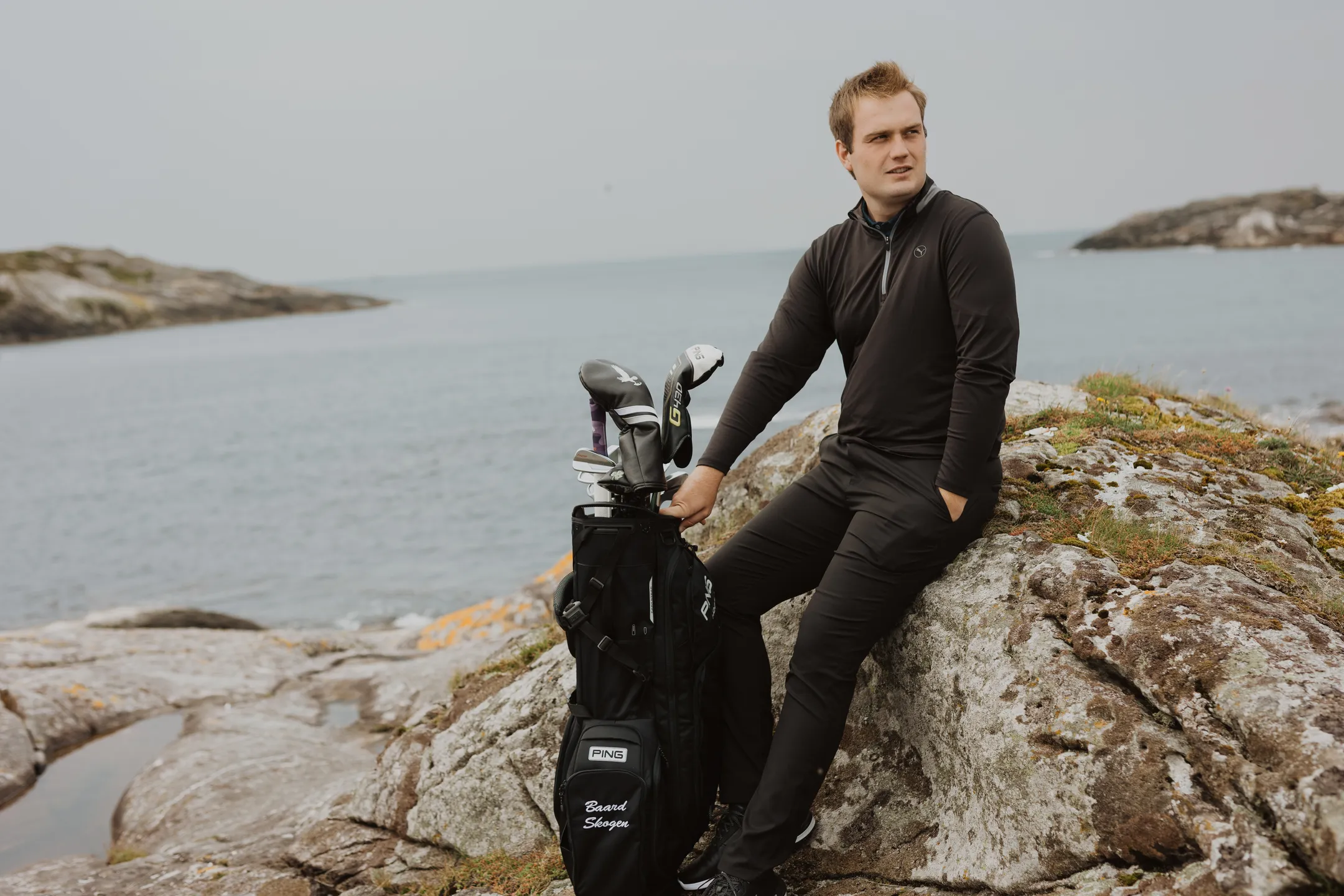 Bård sitting on a smooth seaside rock with his golf equipment