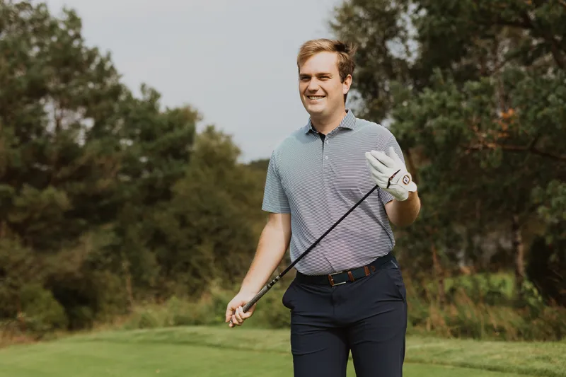 Bård standing next to his golf bag holding an iron club in both hands