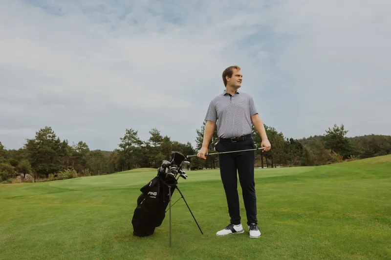 Bård standing next to his golf bag holding an iron club in both hands