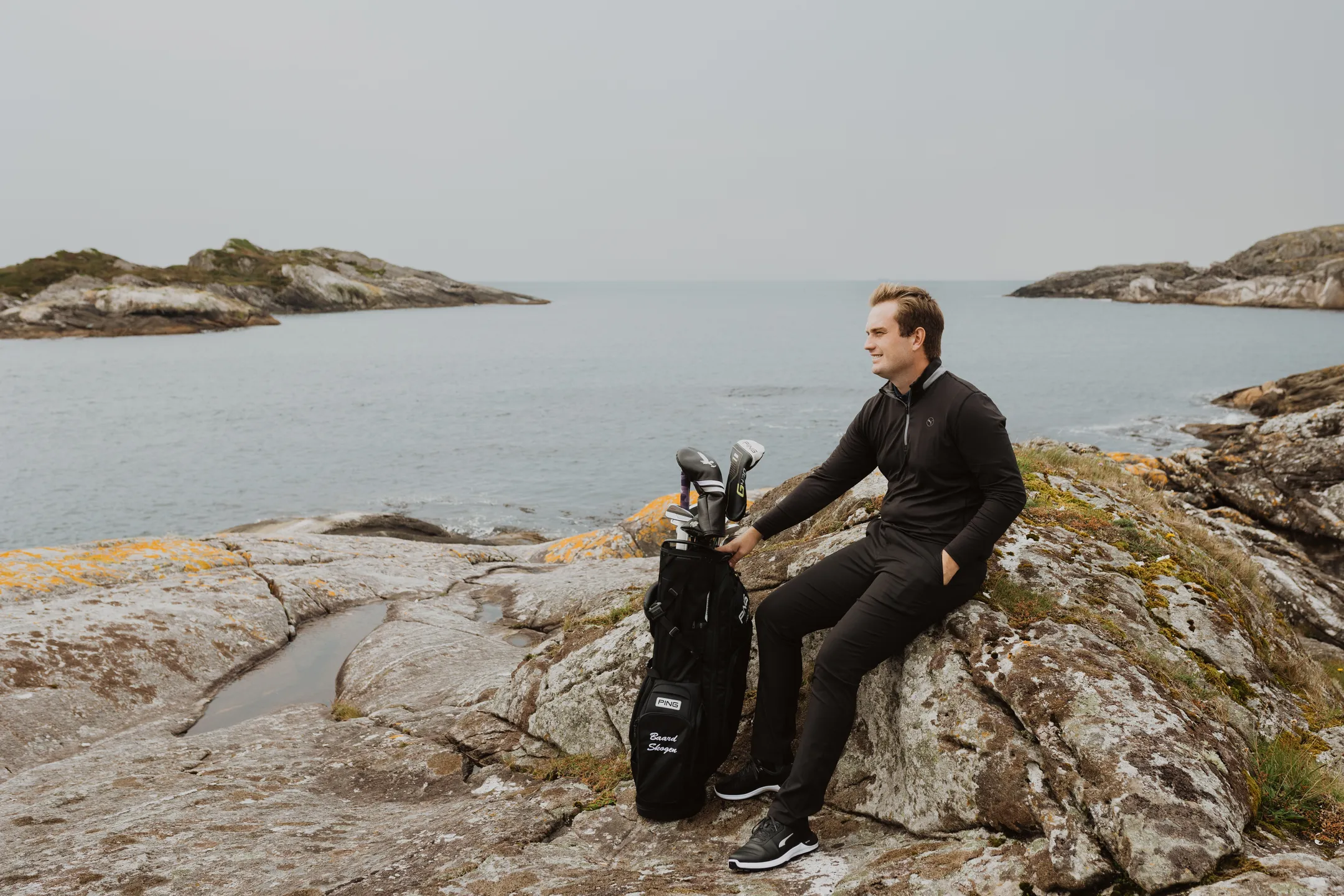 Bård sitting on a smooth seaside rock with his golf equipment